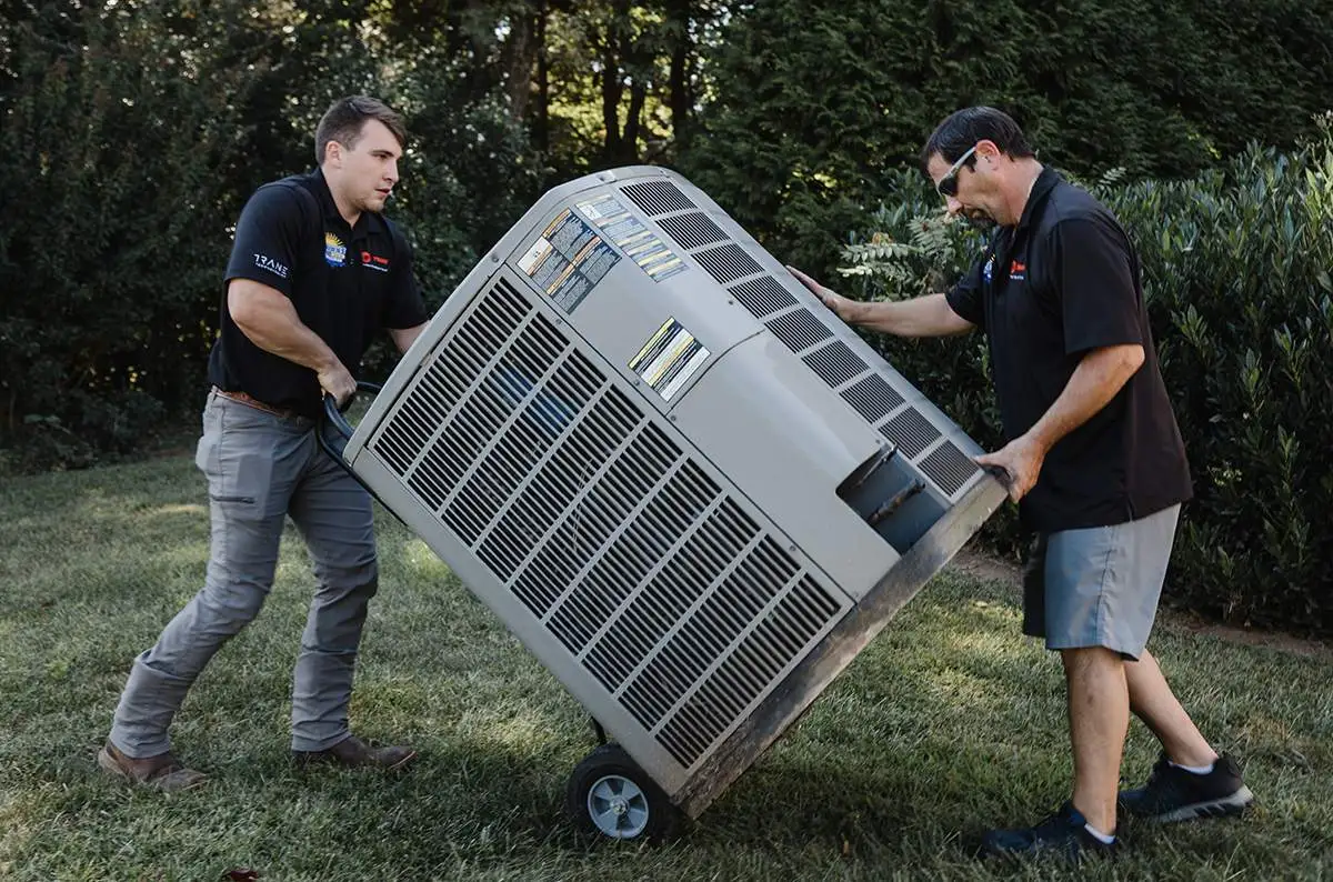 Two HVAC pros moving AC unit on dolly